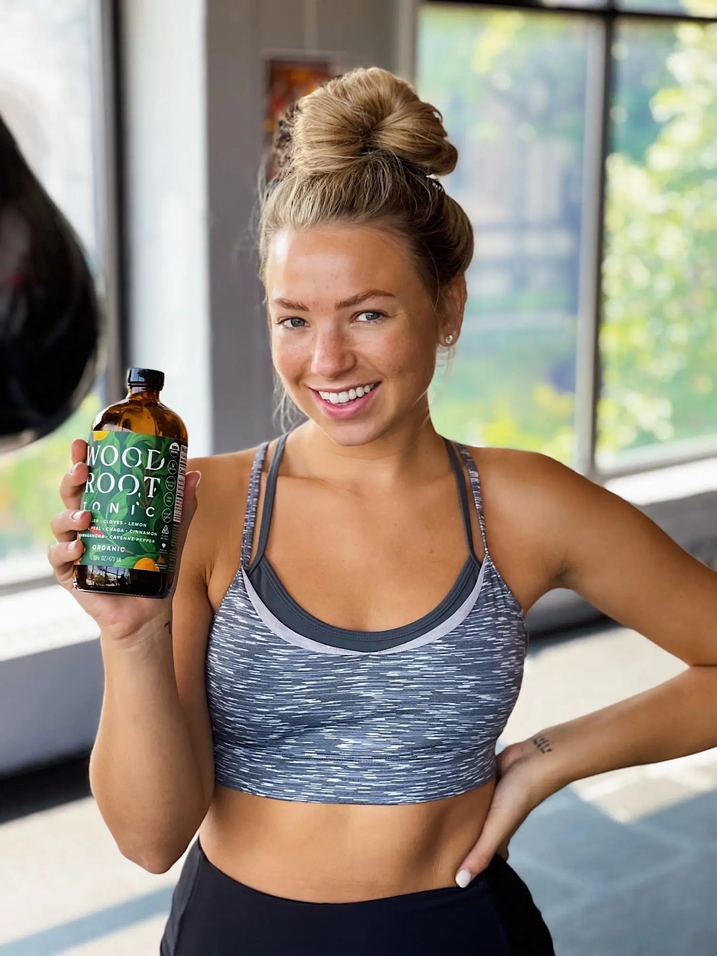 Fit woman smiling holding a bottle of Morningside Naturals Woodroot Tonic.