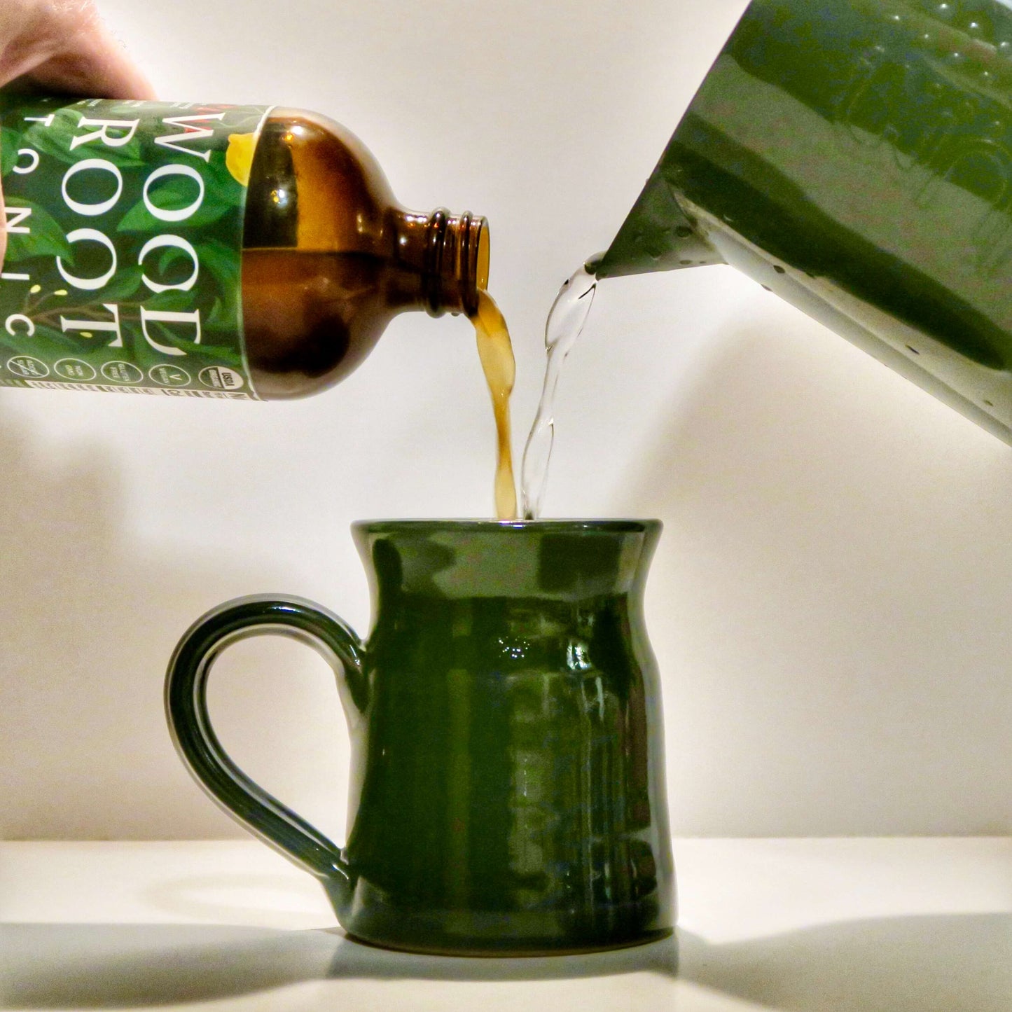 Woodroot Tonic shot being added to warm water to create an herbal tonic perfect for calming stress and anxiety.