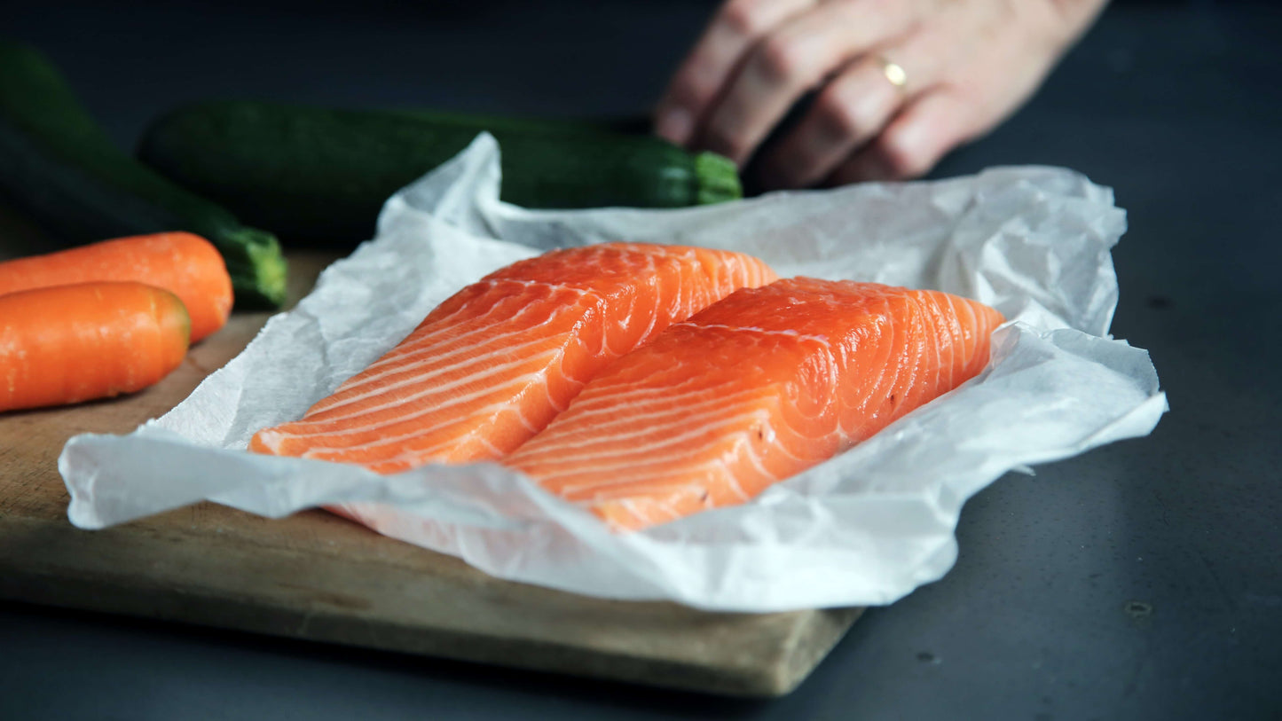 Fresh salmon fillet on parchment with carrots and zucchini in the background on a cutting board, symbolizing nutritious foods that promote gut health.