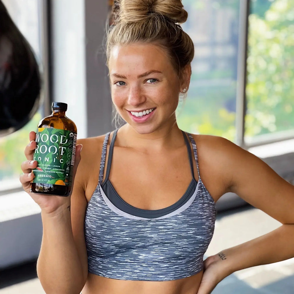 Fit woman smiling holding a bottle of Morningside Naturals Woodroot Tonic.