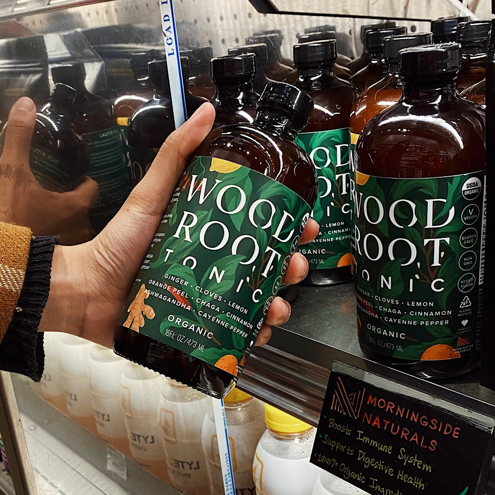Hand picking up Woodroot Tonic bottle from the shelves of a store. 