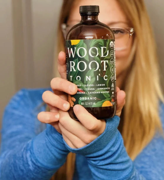Woman presenting a bottle of USDA Organic Woodroot Tonic, highlighting its gut health benefits.