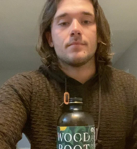 Man taking a selfie with a bottle of Morningside Natural's Woodroot Tonic. 