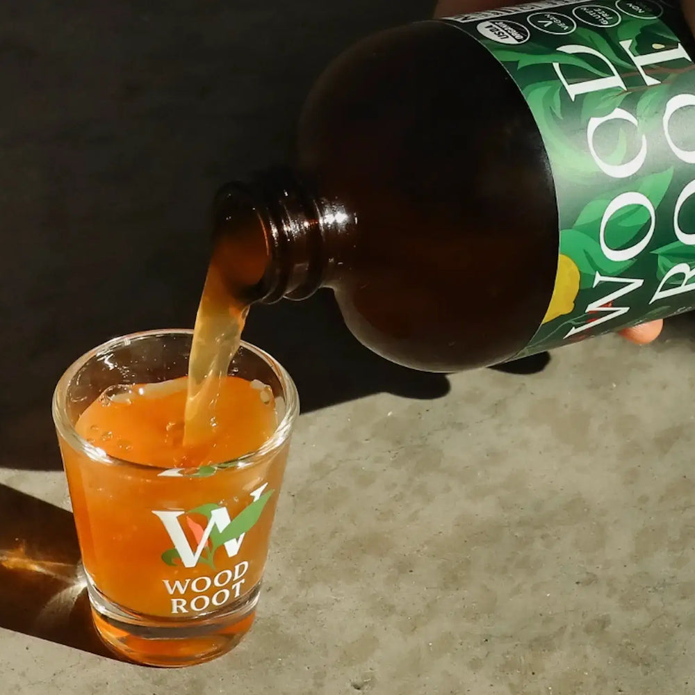 Hand pouring Woodroot Tonic gut shot into shot glass.