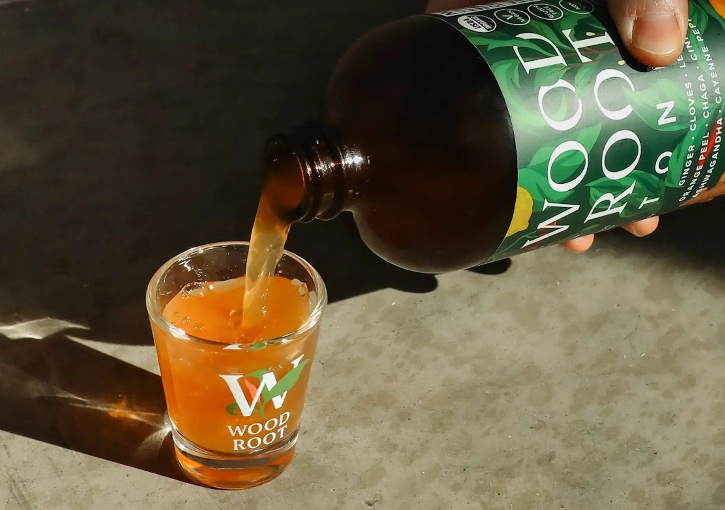 Hand pouring Woodroot Tonic gut shot into shot glass.
