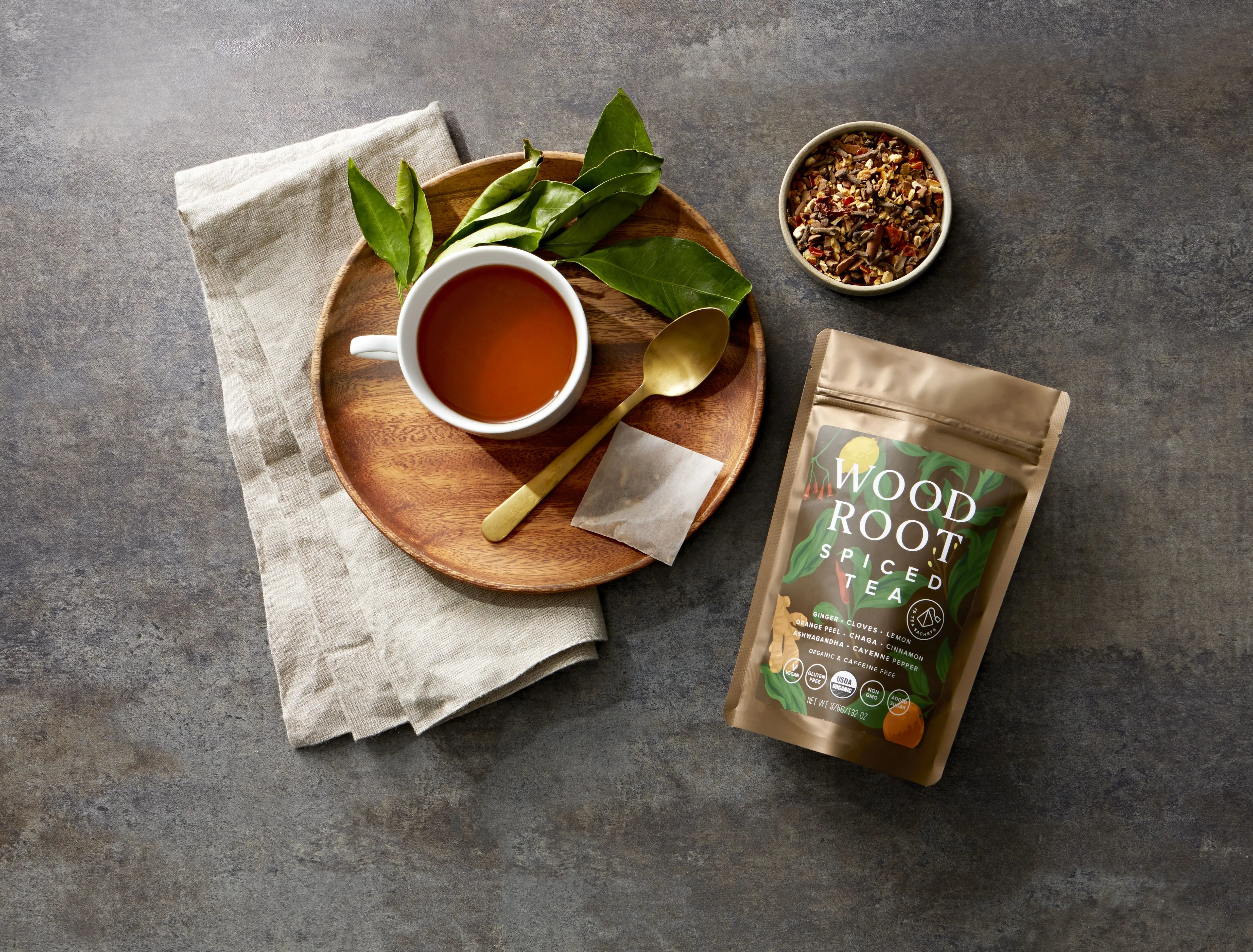 Woodroot Spiced Tea bag next to brewed cup of tea with lose leaf tea in a bowl.