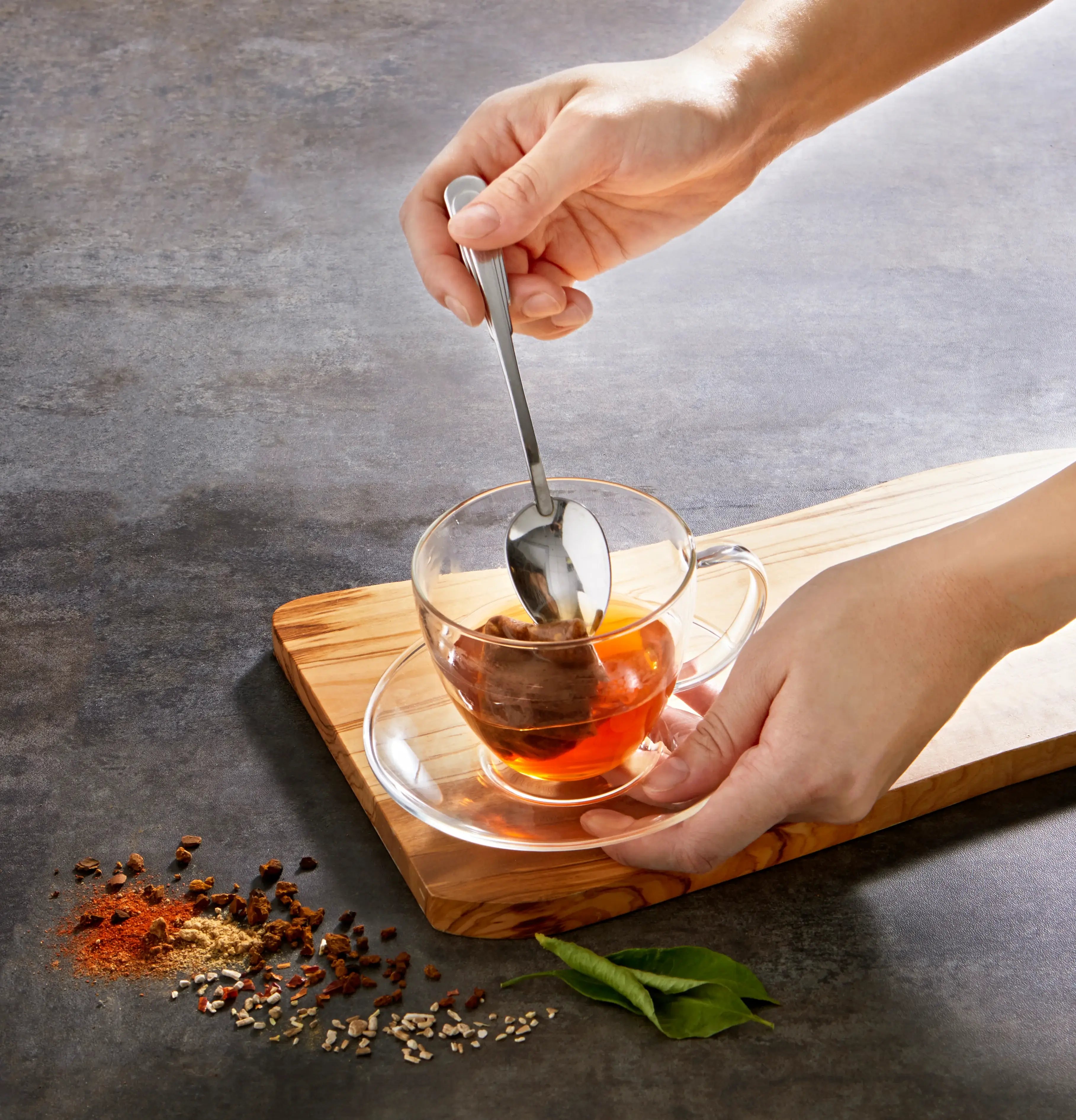 Hand using spoon to pull tea bag out of tea cup.