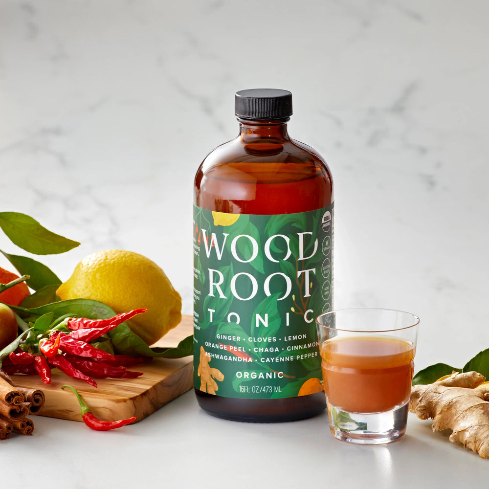 Woodroot Tonic bottle with gut shot already poured in glass shooter, surrounded by usda organic ingredients. 