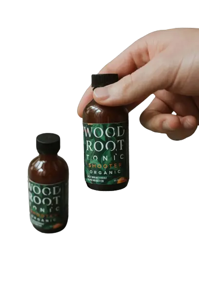 
                  
                    Hand holding single serving shooter bottle of woodroot tonic.
                  
                