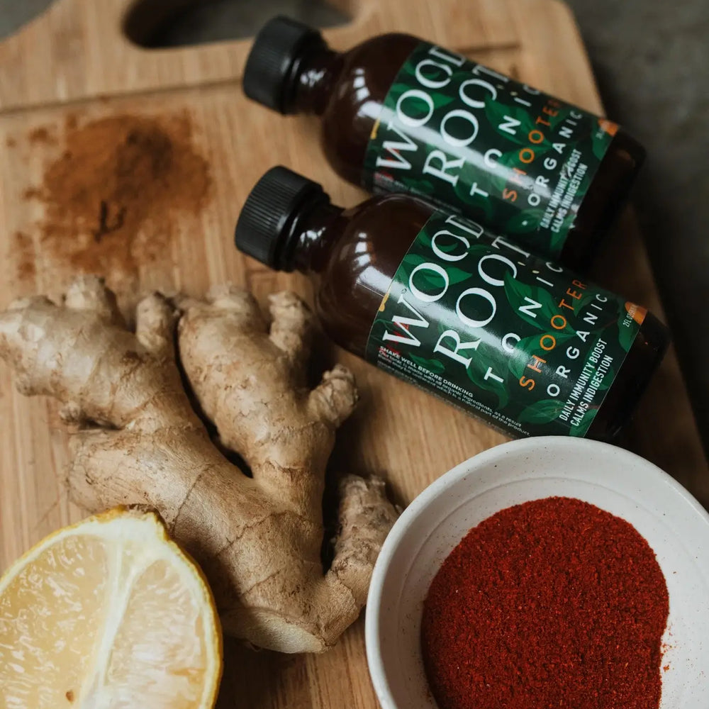 Woodroot Tonic shooters next to key ingredients; ginger, lemon, and cayenne. 