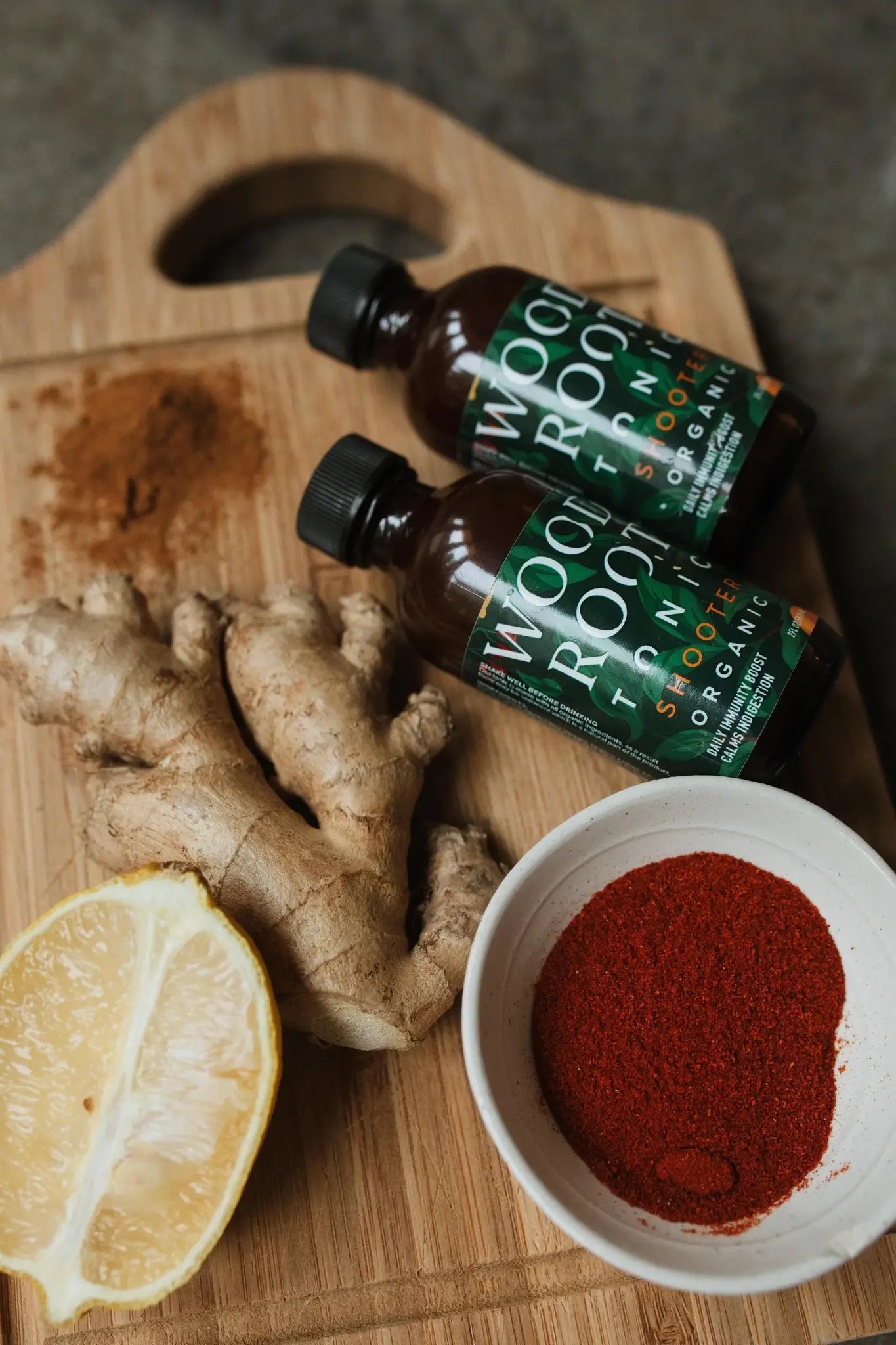 Woodroot Tonic shooters next to key ingredients; ginger, lemon, and cayenne. 