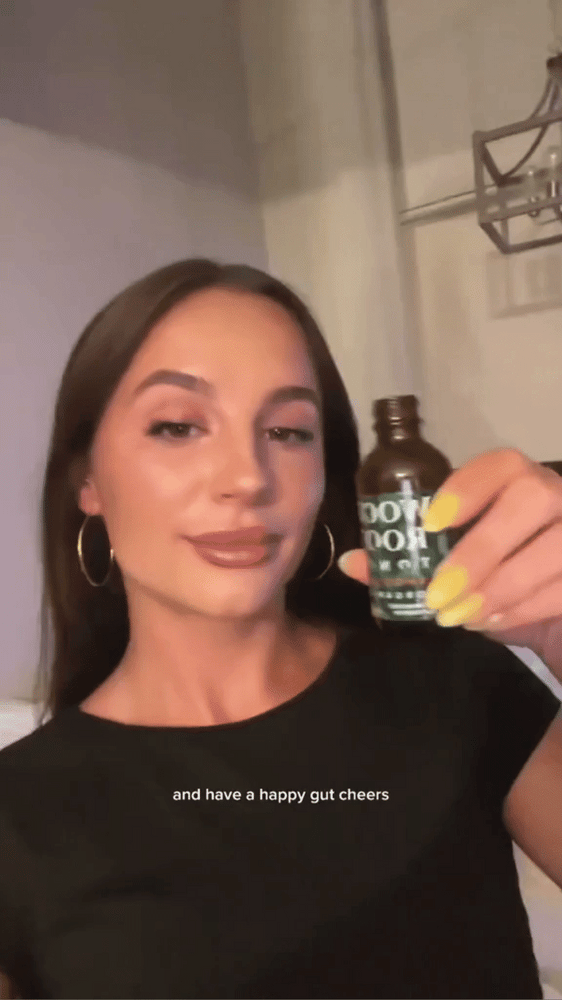 Video of woman doing a cheers and taking a Woodroot Tonic Single Serving Shooter, perfect for on the go gut health.
