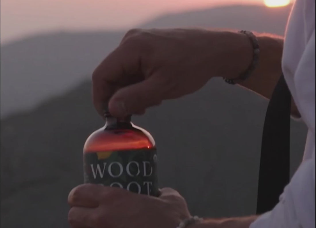 Man opening bottle of Woodroot Tonic and taking a shot while outside over looking the sunset. 