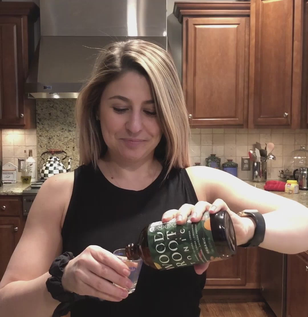 Woman pouring and taking a shot of Morningside Natural's Woodroot Tonic for gut health.