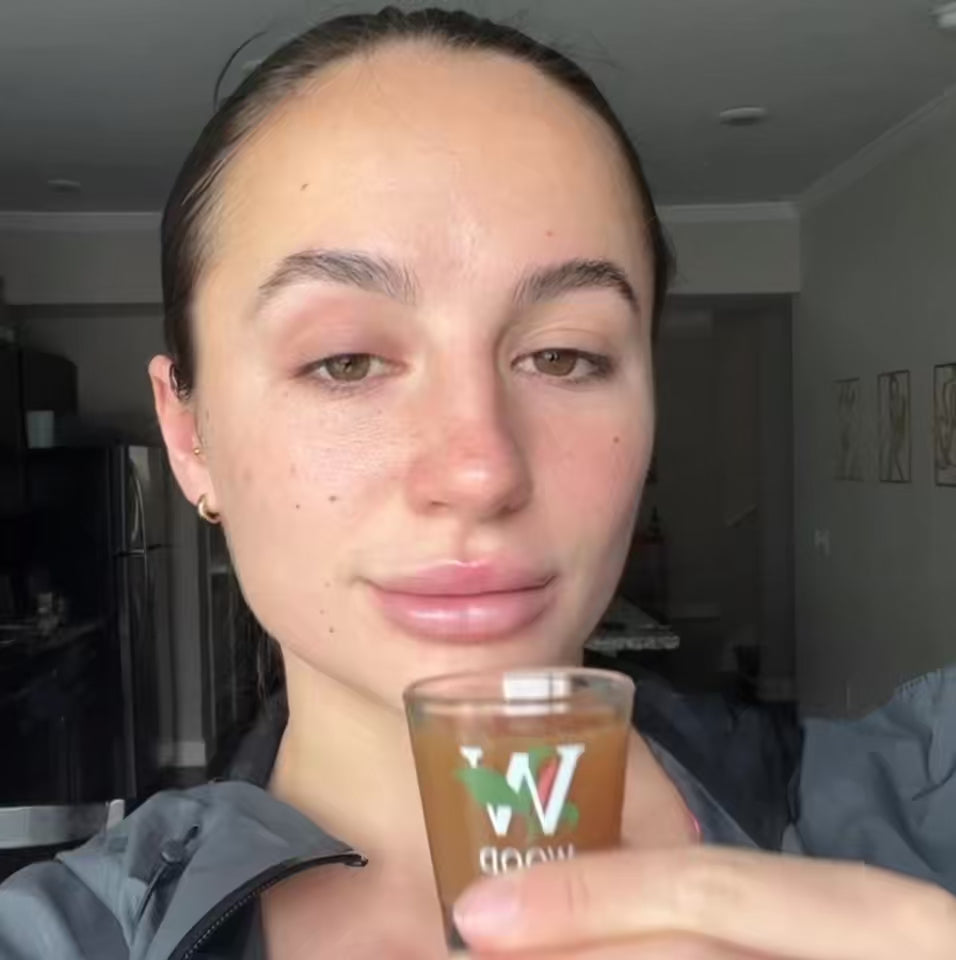Woman taking a shot of Woodroot Tonic to support overall health and wellbeing.