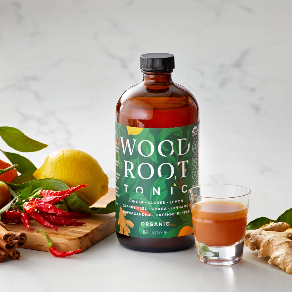 USDA Organic Woodroot Tonic bottle with a wellness shot and ingredients like lemon, apple, cinnamon, and ginger on a marble surface.